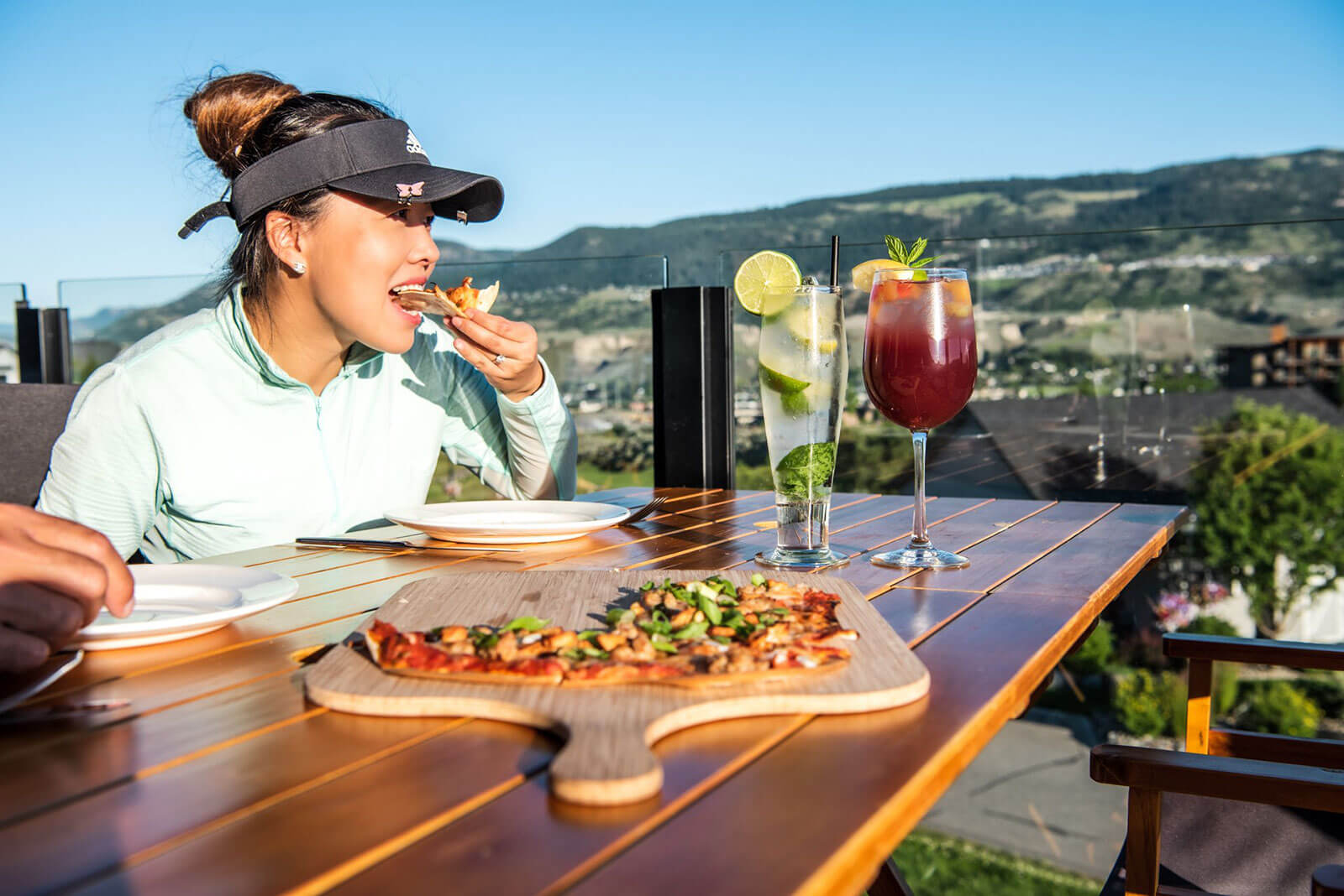 Golfer enjoying pizza and drinks on a scenic patio overlooking Kamloops valley and golf course