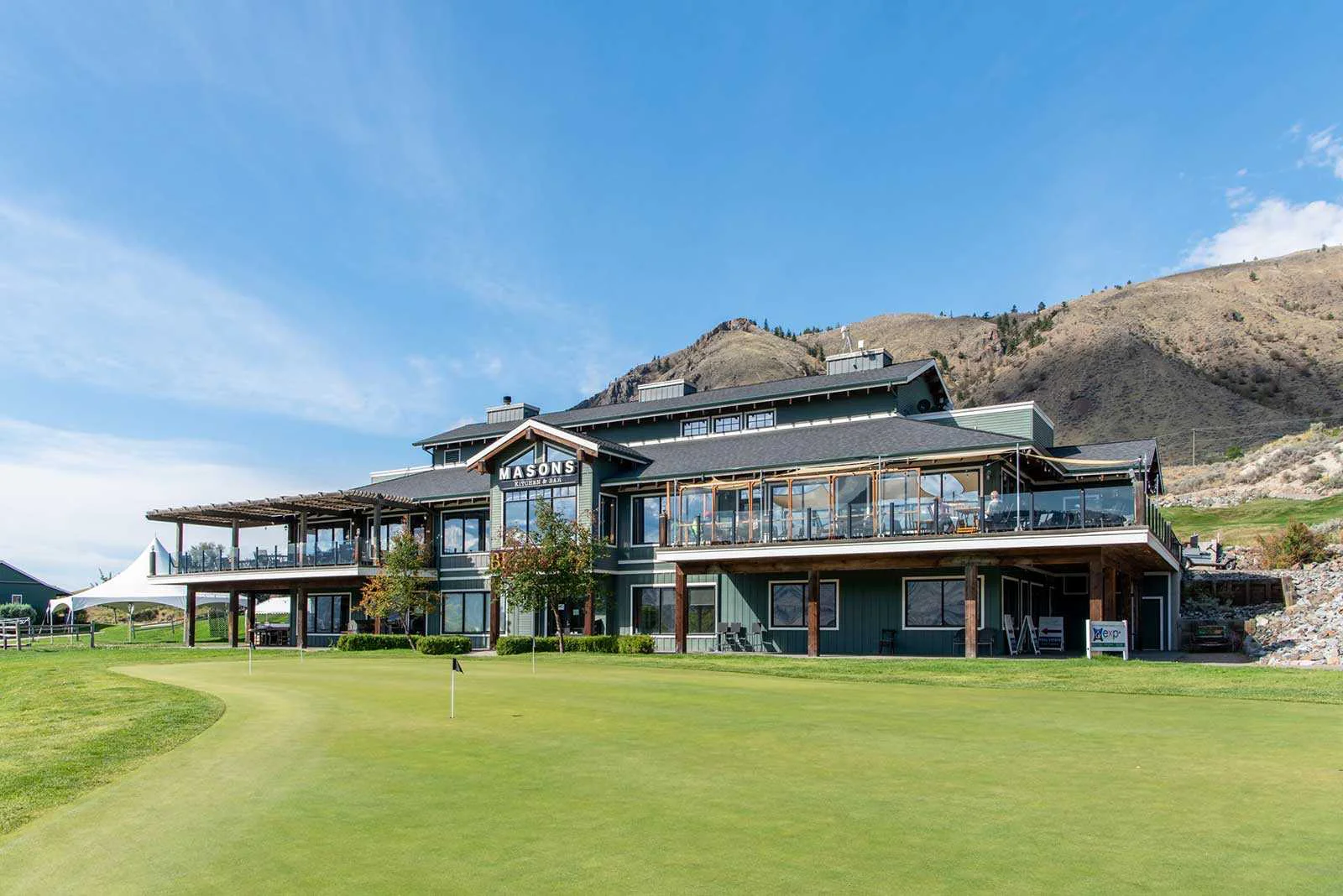 Modern golf clubhouse with patio dining overlooking green and Kamloops hillside landscape