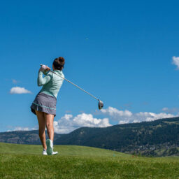 Female golfer following through on a drive with mountain backdrop and clear blue sky