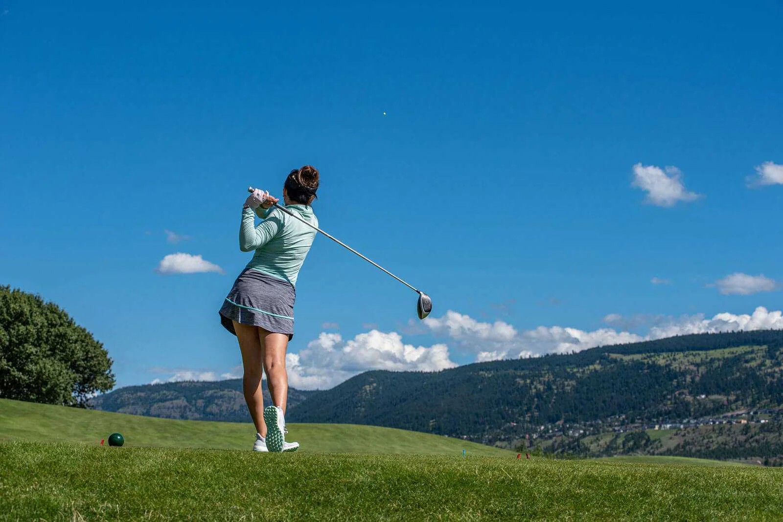 Female golfer following through on a drive with mountain backdrop and clear blue sky
