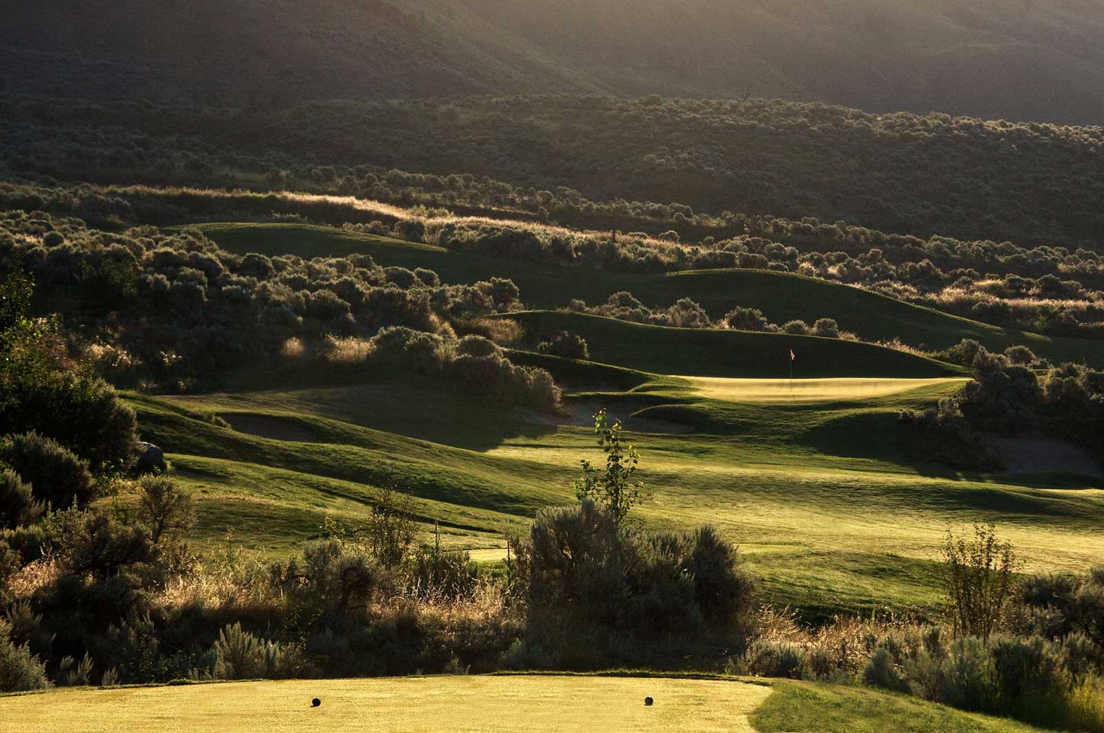 Golden hour view of rolling golf course fairways and green surrounded by Kamloops hillside landscape