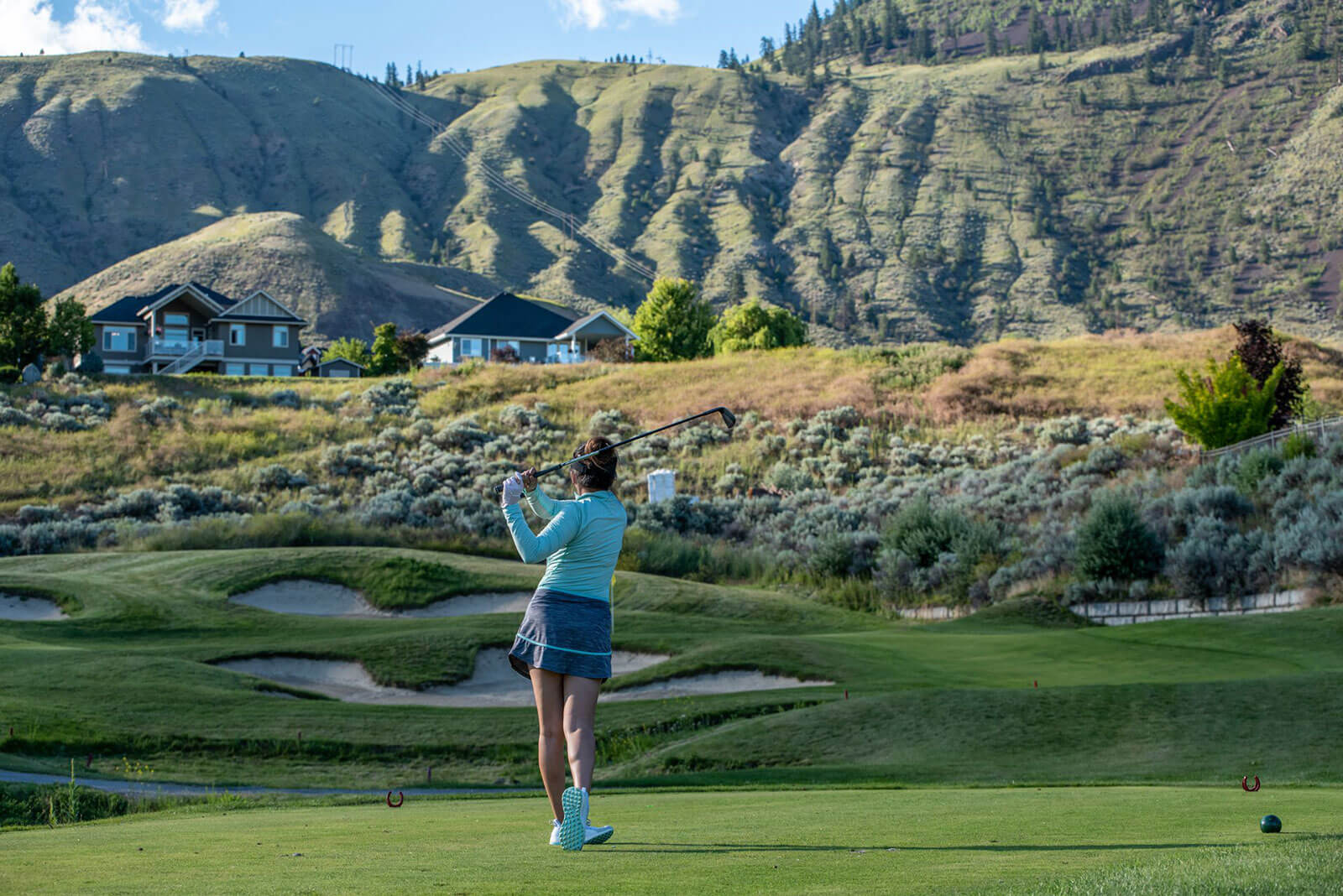 Female golfer teeing off at Bighorn Golf Course with Kamloops hills and desert landscape backdrop