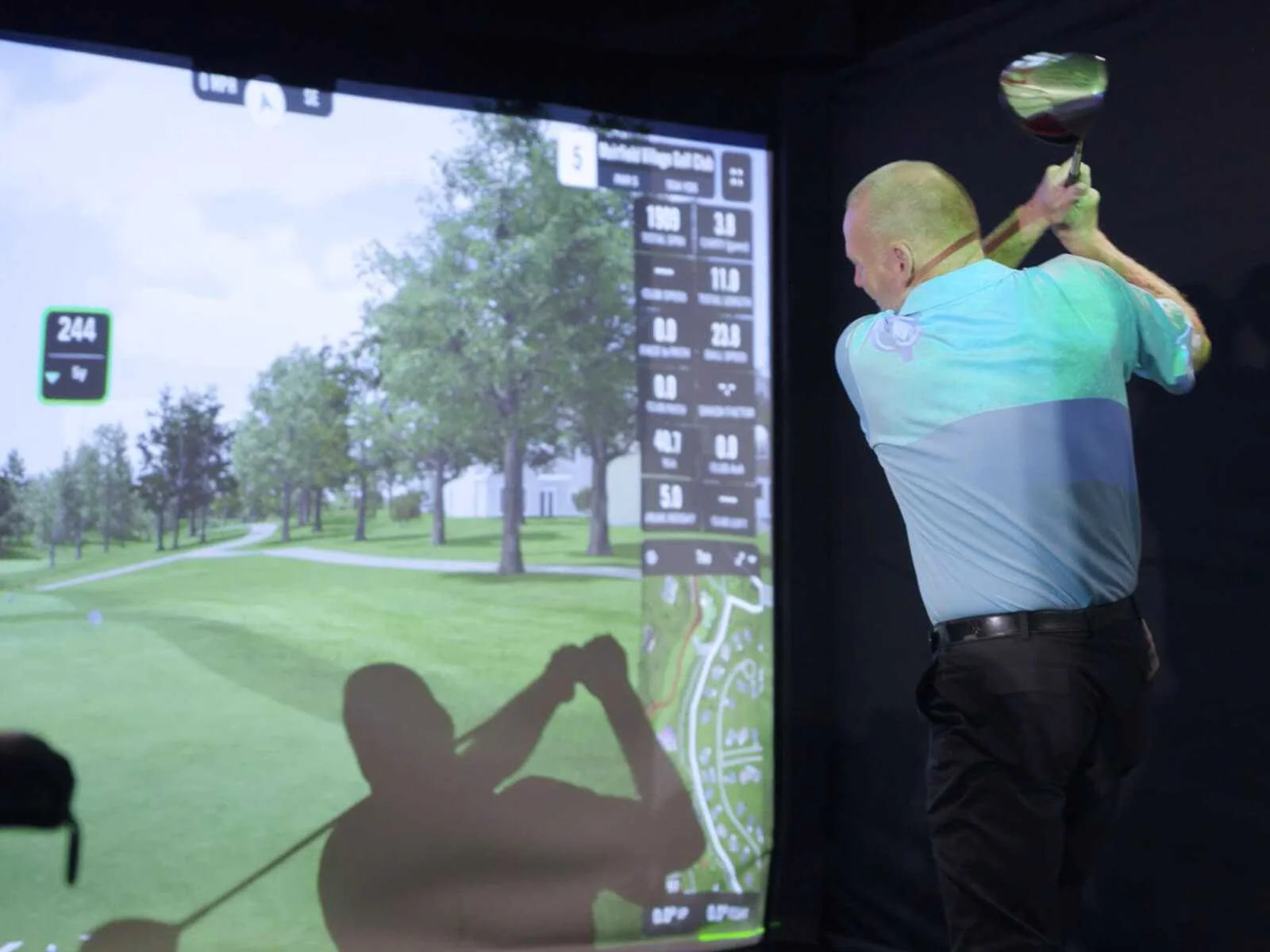 Golfer swinging a driver at a high-tech indoor golf simulator in Kamloops.