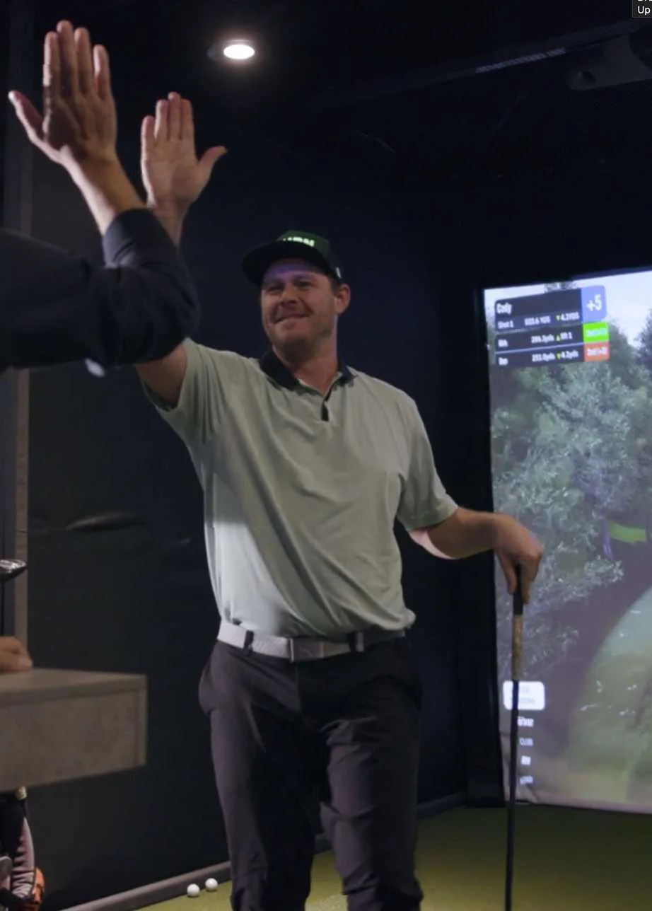 Golfers celebrating with a high-five at an indoor golf simulator in Kamloops.