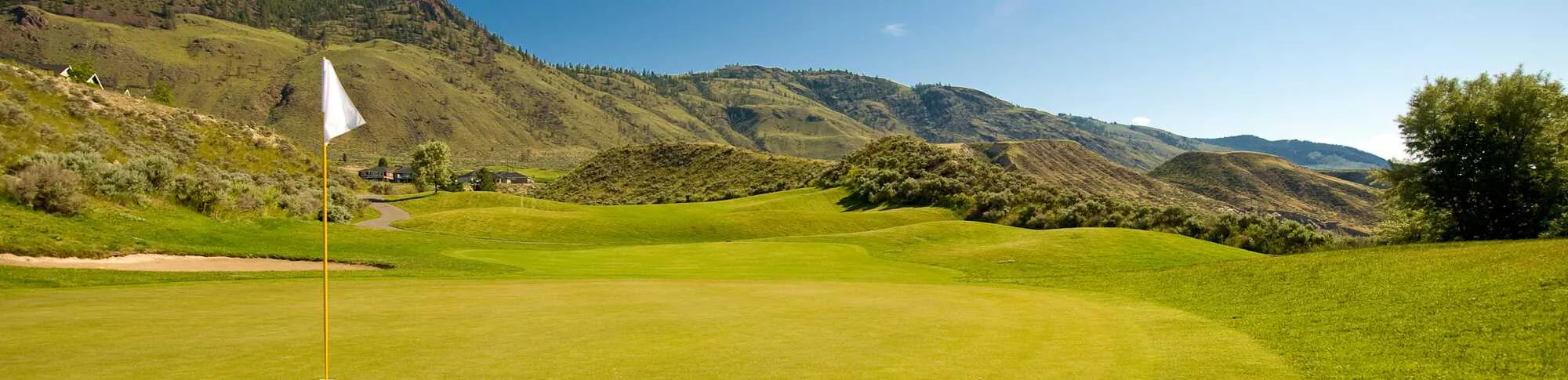 Golf green with flagstick at Bighorn Golf Course, surrounded by rolling hills and Kamloops landscape