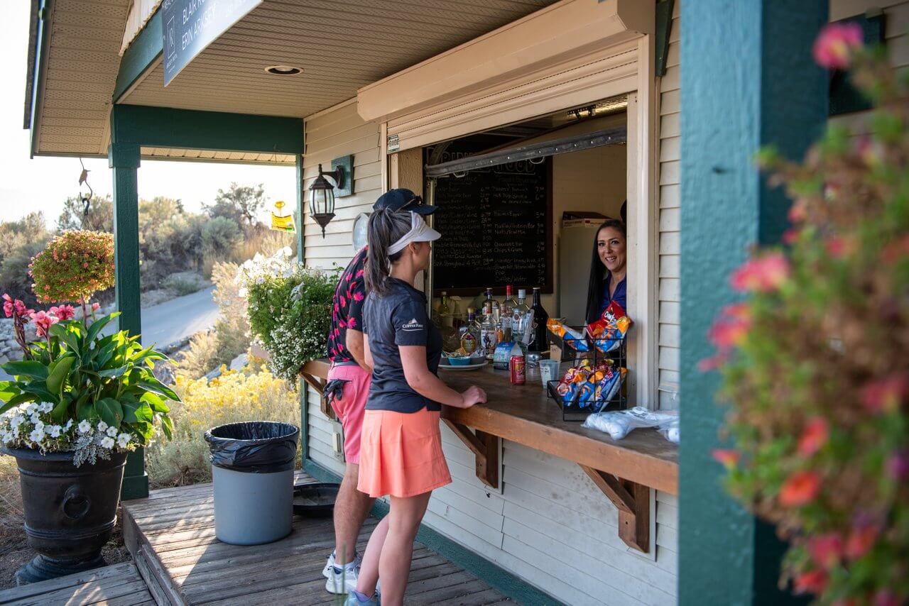 Golfers ordering snacks and drinks at course halfway house window with outdoor setting