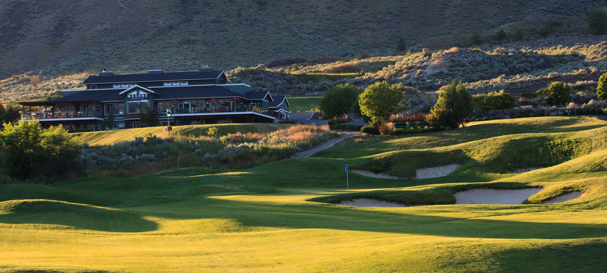 Golf course green and fairways at sunset with clubhouse and patio overlooking Kamloops hillside