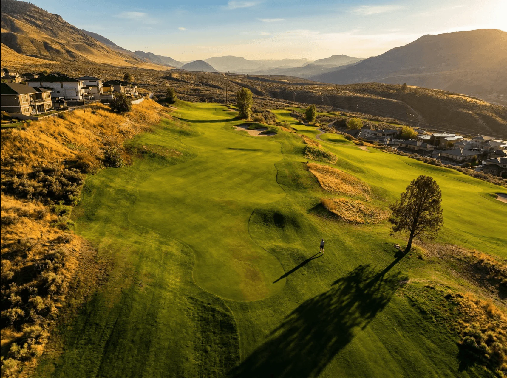 Aerial view of fairway and green at Bighorn Golf Kamloops with lone golfer and surrounding valley hills