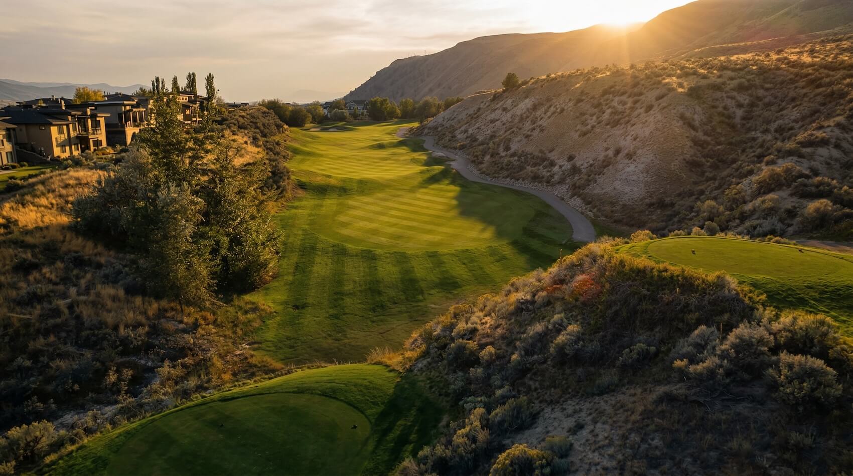 Elevated tee shot view of narrow fairway winding through hills at Bighorn Golf Kamloops at sunset