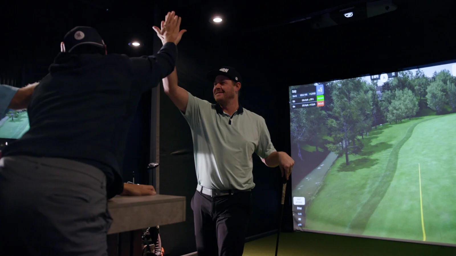 Golfers celebrating with a high five after a successful shot in indoor golf simulator lounge