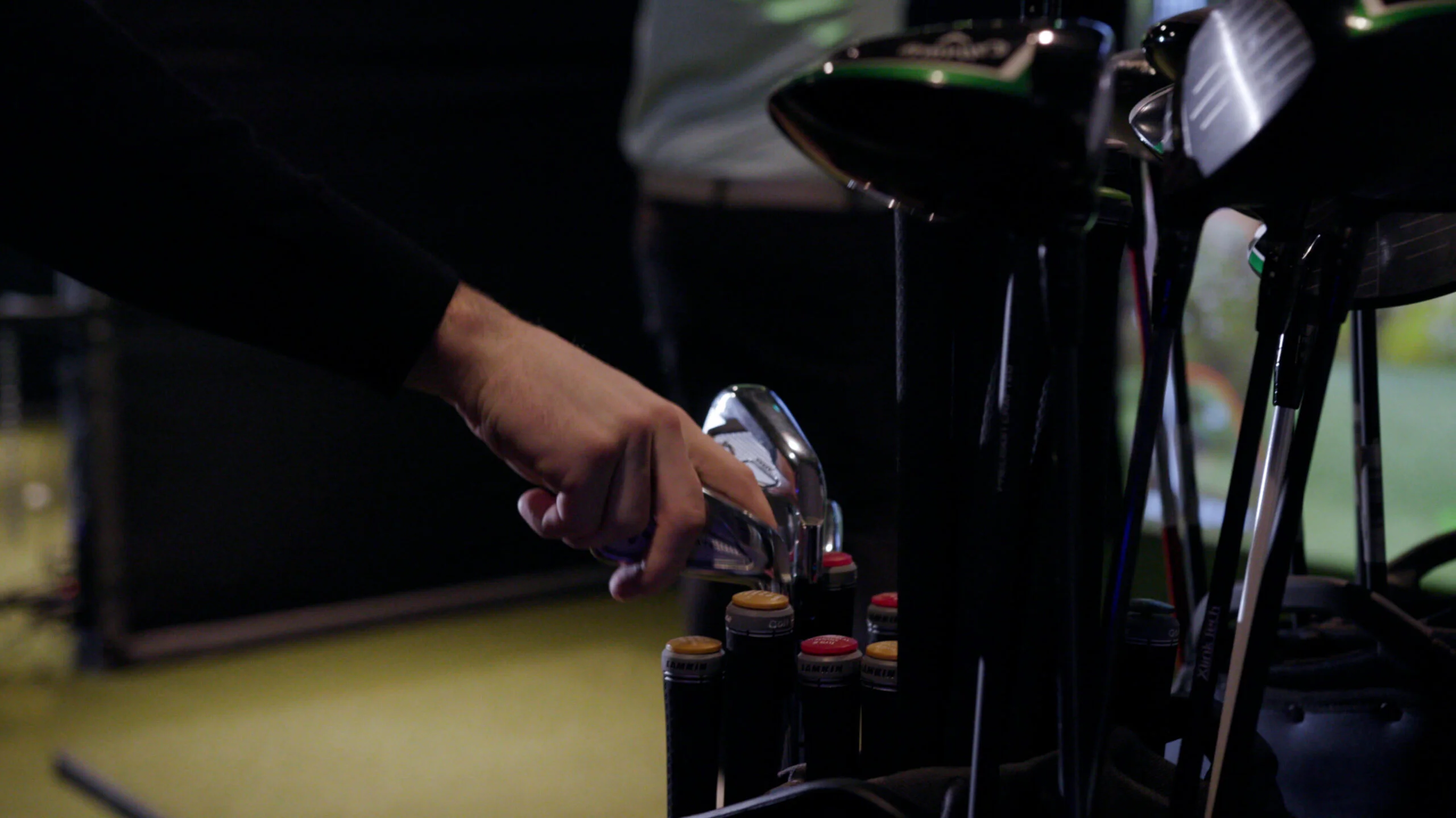 Hand selecting a golf club from a bag inside an indoor golf simulator facility