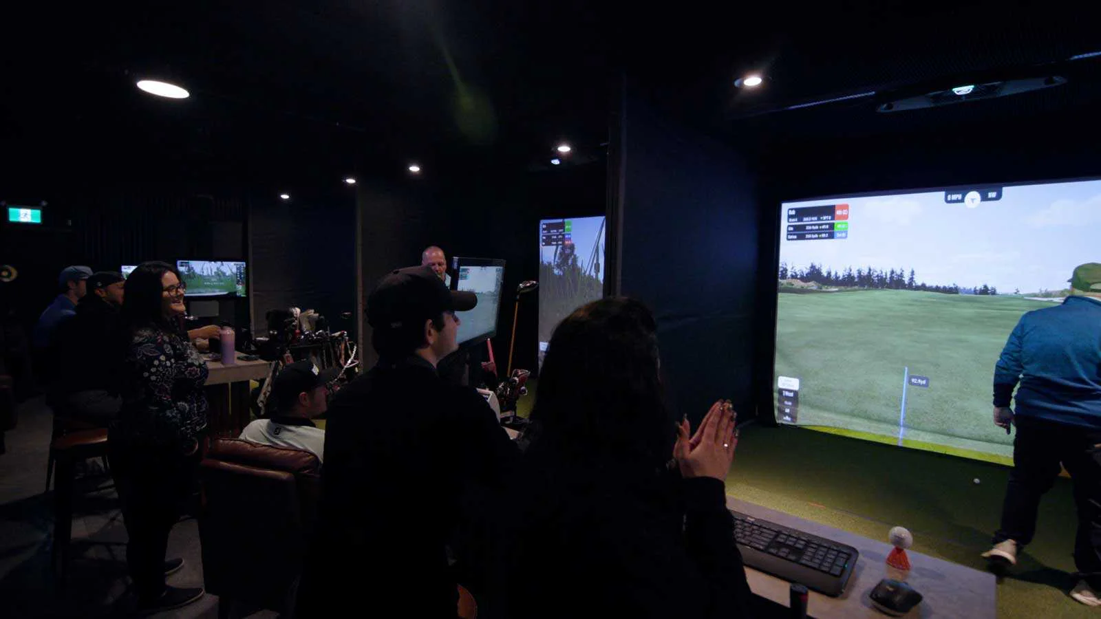 Group enjoying indoor golf simulator experience with virtual course display and social atmosphere