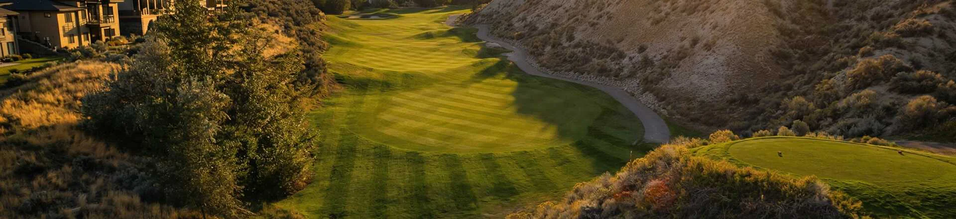 Elevated view of striped fairway winding through hills at Bighorn Golf Kamloops during golden hour