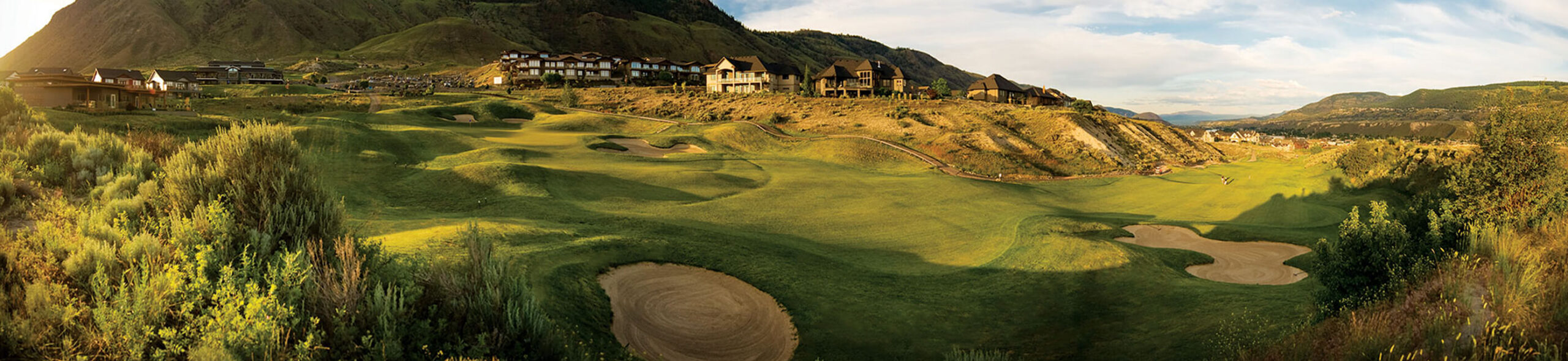 Wide fairway view at Bighorn Golf Kamloops with hillside homes, sculpted bunkers, and mountain backdrop