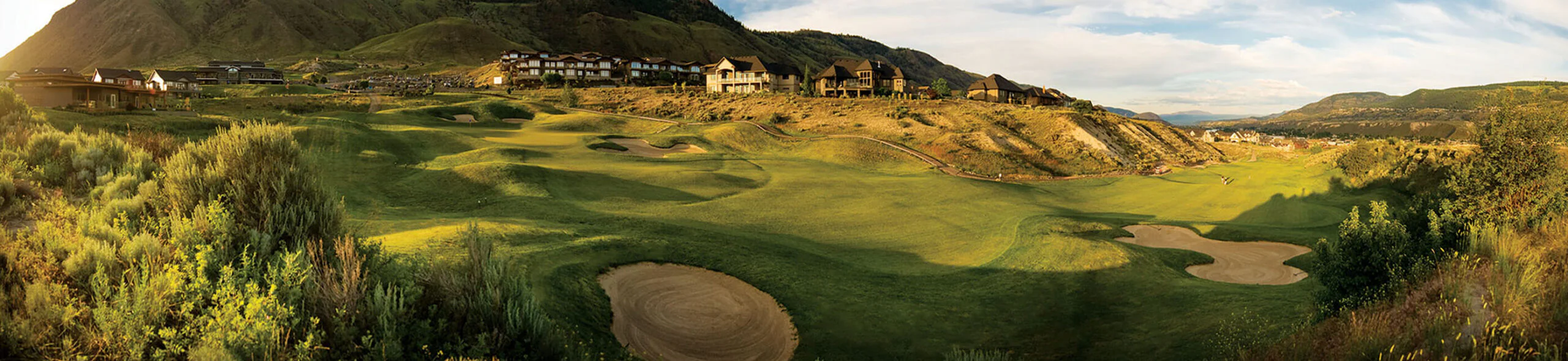 Wide fairway view at Bighorn Golf Kamloops with hillside homes, sculpted bunkers, and mountain backdrop