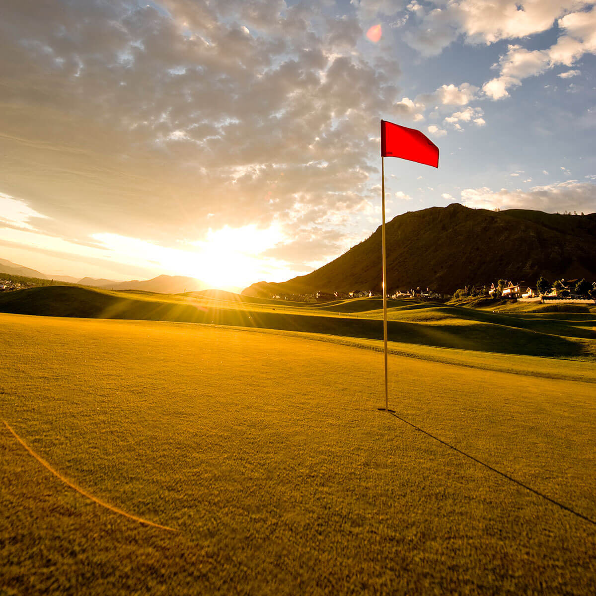 Red flag on sunlit green at Bighorn Golf Kamloops during golden hour with mountain backdrop